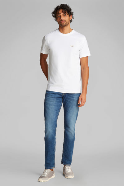 Wit T-shirt met korte mouwen van Calvin Klein, gedragen met een blauwe spijkerbroek en grijze sneakers.