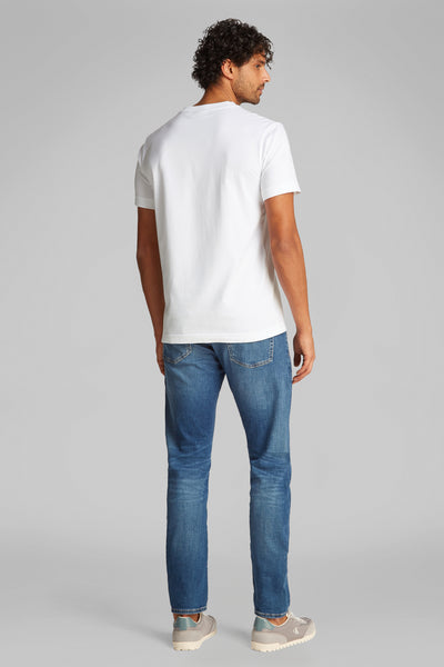 T-shirt blanc à manches courtes de Calvin Klein, porté avec un jean bleu et des baskets grises.