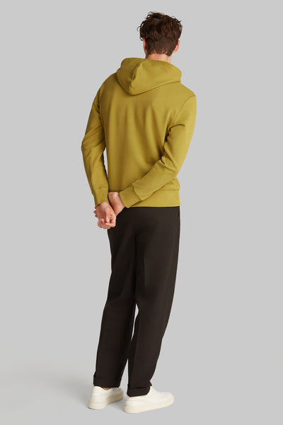 Sweat à capuche ocre de Calvin Klein, avec poignets côtelés, porté avec un pantalon noir et des baskets blanches.