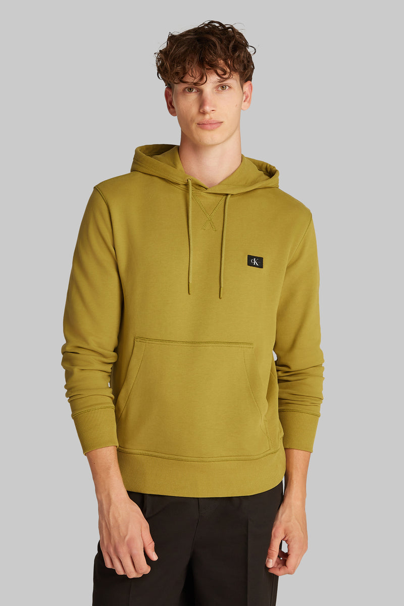 Sweat à capuche ocre par Calvin Klein, avec cordon de serrage et poche kangourou, porté avec un pantalon noir.
