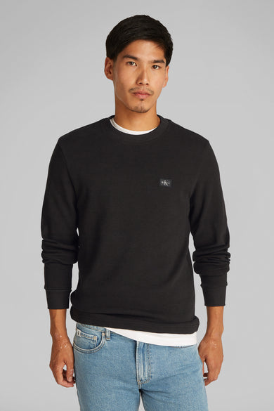 T-shirt à manches longues noir de Calvin Klein, porté avec un t-shirt blanc et un jean bleu clair.
