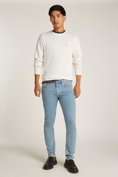 T-shirt écru à manches longues de Calvin Klein, porté avec un jean bleu et des mocassins noirs.