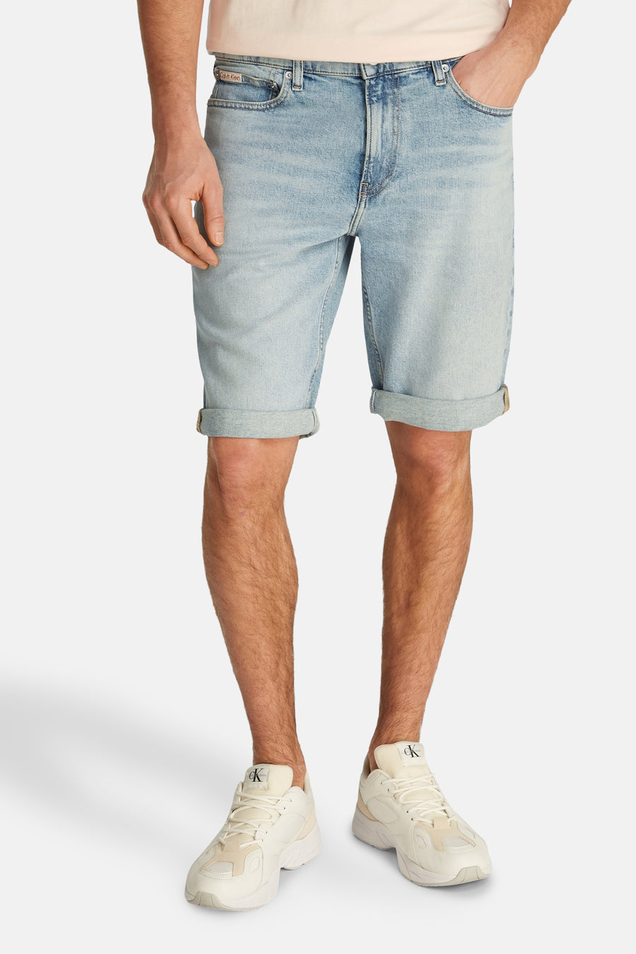 Korte lichtblauwe spijkerbroek van Calvin Klein, gedragen met een roze T-shirt en sportschoenen.