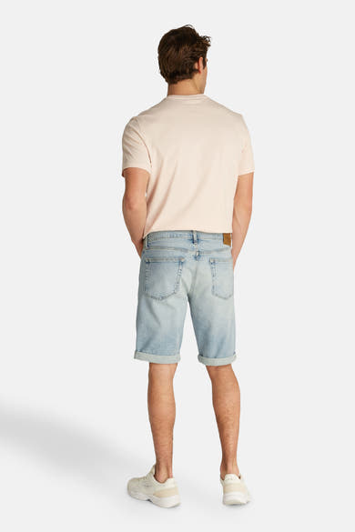 Short en jeans denim bleu clair de Calvin Klein, porté avec un t-shirt rose et des chaussures de sport.