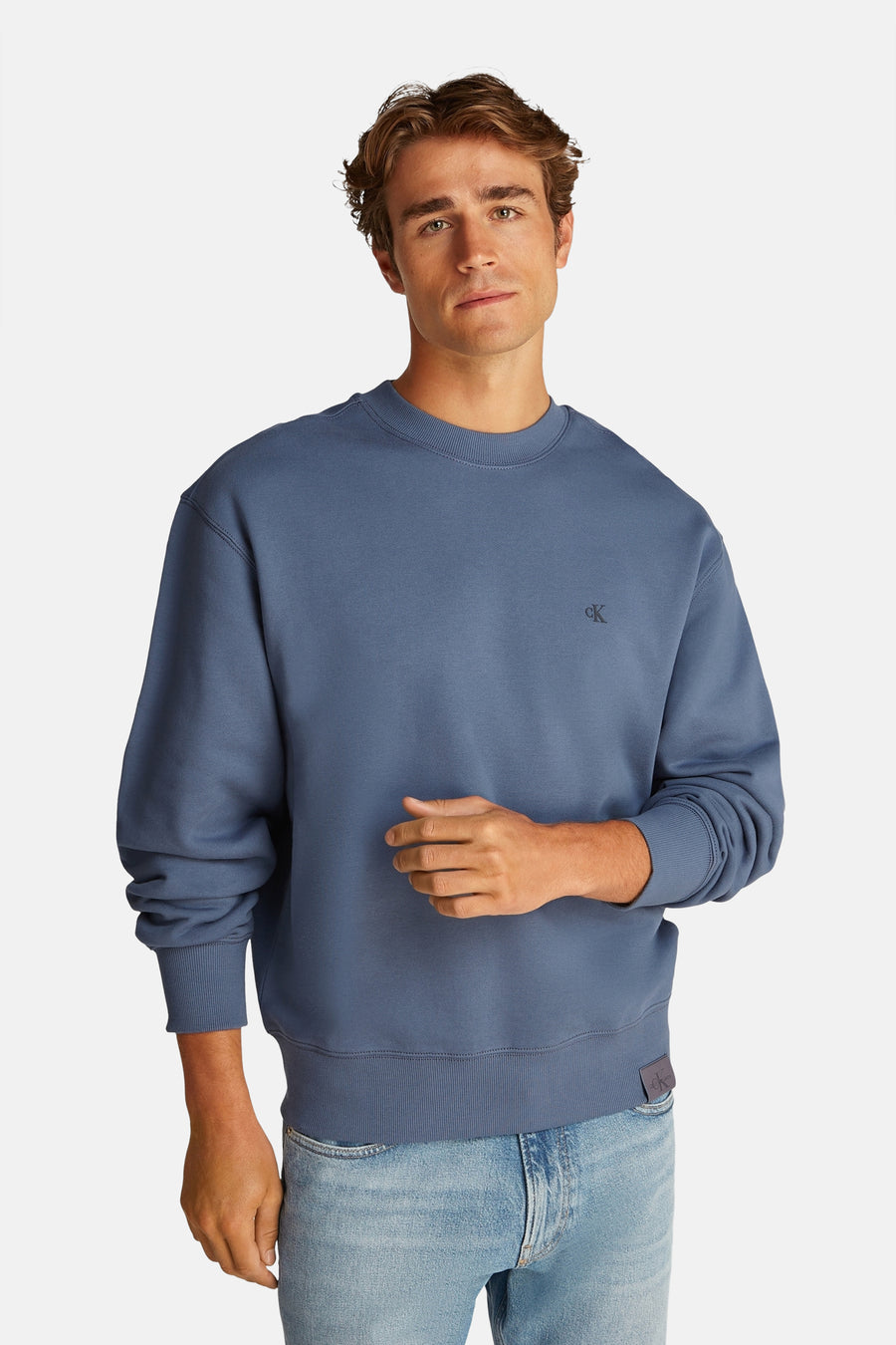 Sweat-shirt bleu encolure ronde de Calvin Klein, avec un petit logo sur le devant et porté avec un jean clair.