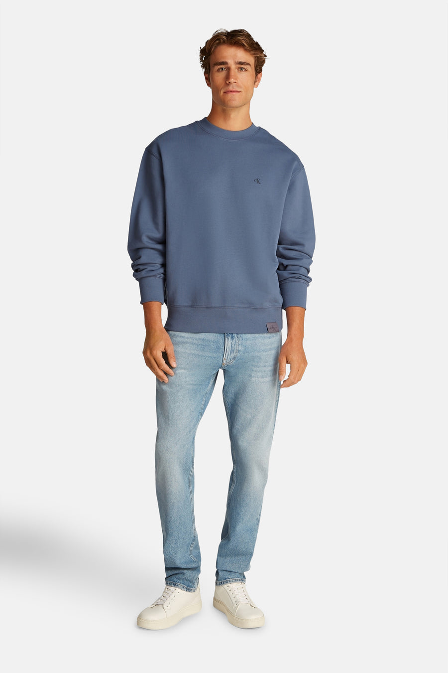 Sweat bleu par Calvin Klein, porté avec un jean clair et des baskets blanches.