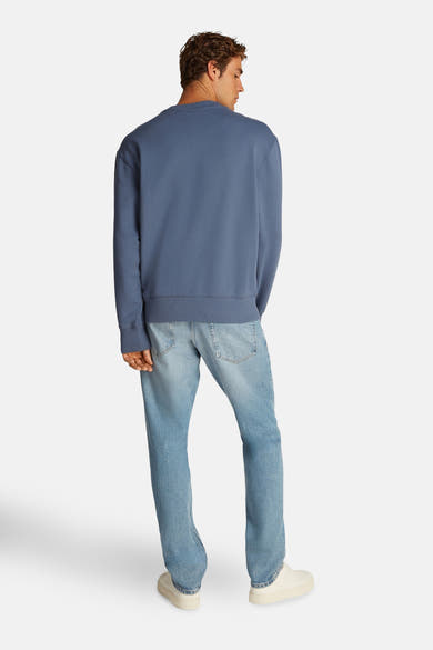 Sweat-shirt bleu de Calvin Klein, porté avec un jean délavé et des baskets blanches, vue de dos.
