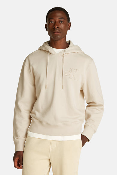 Beige Calvin Klein hoodie, met capuchon, gedragen over een wit T-shirt en een beige joggingbroek.
