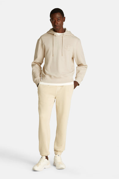 Beige Calvin Klein hoodie met logo op de borst, gedragen over een wit T-shirt en een beige joggingbroek.