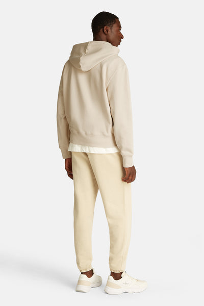 Sweat à capuche beige de Calvin Klein, avec capuche, porté sur un t-shirt blanc et un pantalon de survêtement beige.