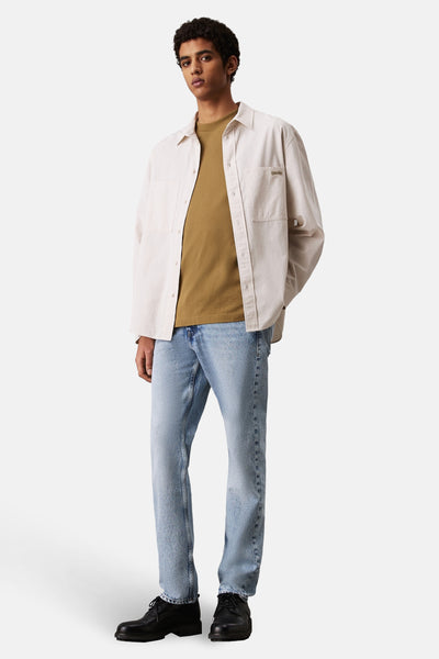 Jean droit en denim bleu clair de Calvin Klein, porté avec une chemise beige et des chaussures noires.
