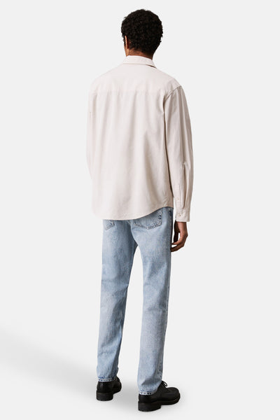 Jean droit en denim bleu clair de Calvin Klein porté avec une chemise écrue et des chaussures noires.
