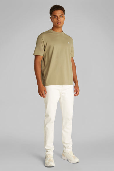 Beige T-shirt met korte mouwen van Calvin Klein, gedragen met een witte broek en beige sportschoenen.