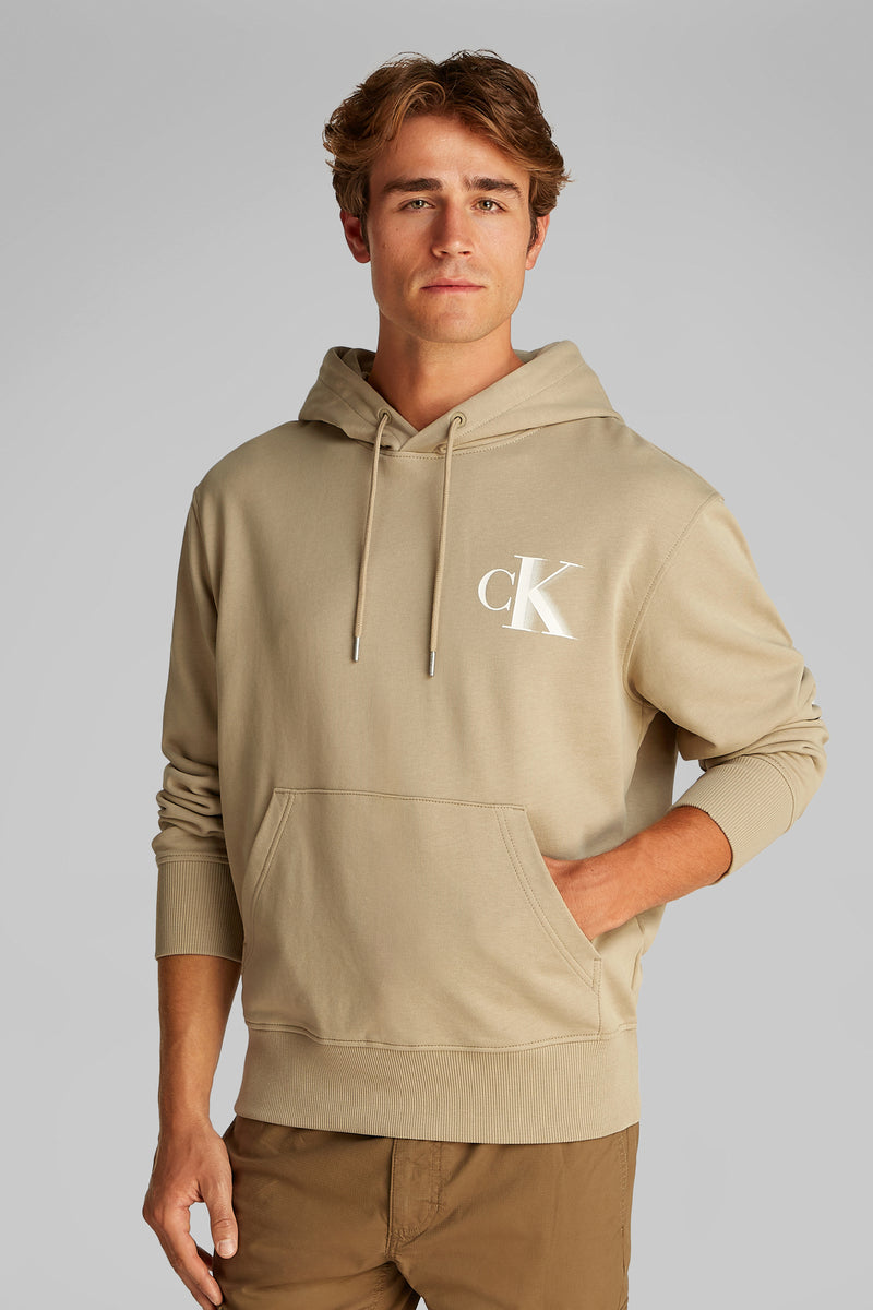 Beige Calvin Klein hoodie met logo op de rug, gedragen met een bruine cargobroek.