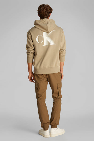 Sweat à capuche beige de Calvin Klein avec logo au dos, porté avec un pantalon cargo marron.