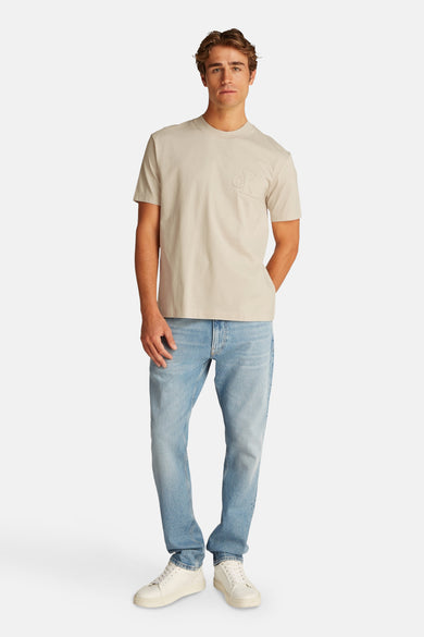 Beige T-shirt met korte mouwen van Calvin Klein, gedragen met een blauwe jeans en witte sneakers.