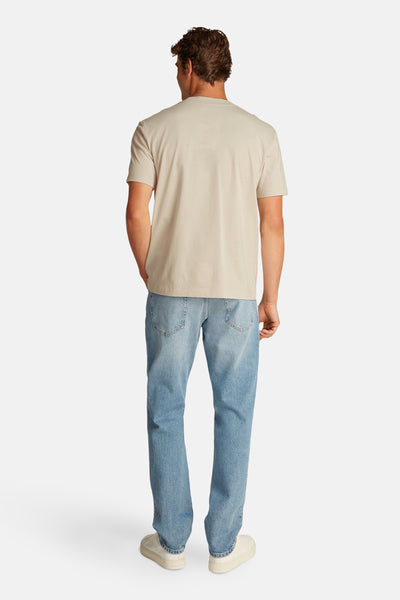 Beige T-shirt met korte mouwen van Calvin Klein, gedragen met een verbleekte spijkerbroek en witte sneakers, achtergezicht.