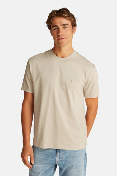 Beige T-shirt met korte mouwen van Calvin Klein, met toon-op-toon logo op de borst, gedragen met een lichtblauwe jeans.