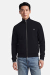 Black zip-front gilet by Fred Perry with white laurel wreath logo, ribbed cuffs and hem, front pockets, worn with light blue jeans in front view.