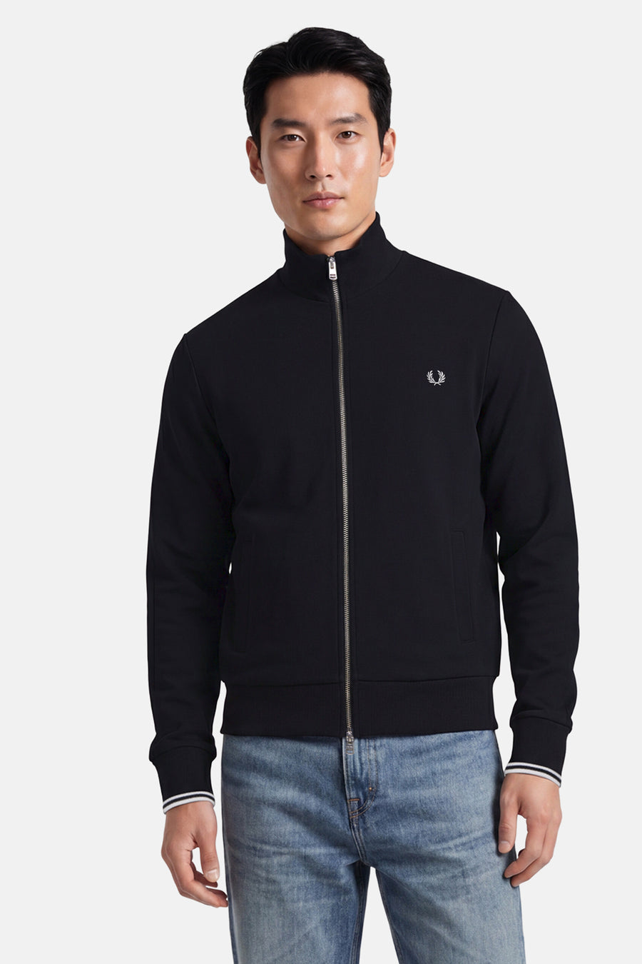 Black zip-front gilet by Fred Perry with white laurel wreath logo, ribbed cuffs and hem, front pockets, worn with light blue jeans in front view.