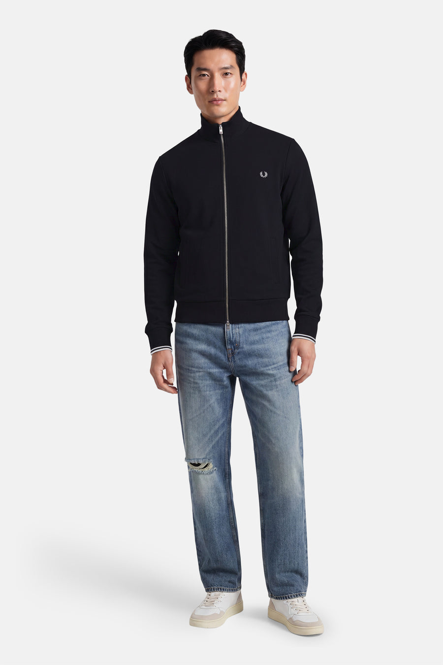 Black zip-front gilet by Fred Perry with ribbed cuffs and chest logo, worn with distressed jeans and white sneakers, full-length front view