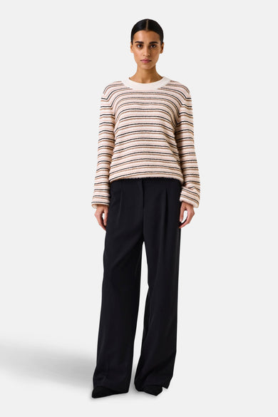 Pull à col rond multicolore de GARCIA, à rayures horizontales beige, marron et noir, porté avec un pantalon noir ample.
