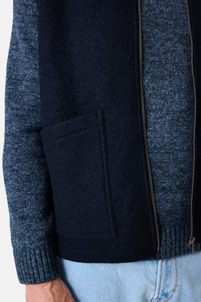 Blauwe bodywarmer van GARCIA met opgestikte zak, gedragen over een gemêleerde blauwe trui en een lichte spijkerbroek.