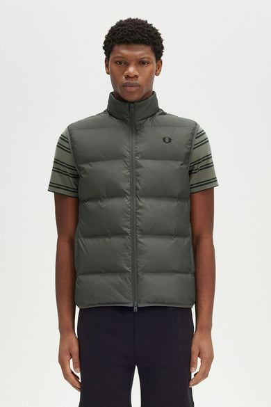 Veste sans manches kaki de Fred Perry, sur un t-shirt rayé et un pantalon noir unis.