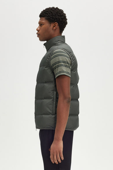 Veste sans manches kaki de Fred Perry, portée sur un t-shirt rayé et un pantalon de survêtement noir, vue de côté.