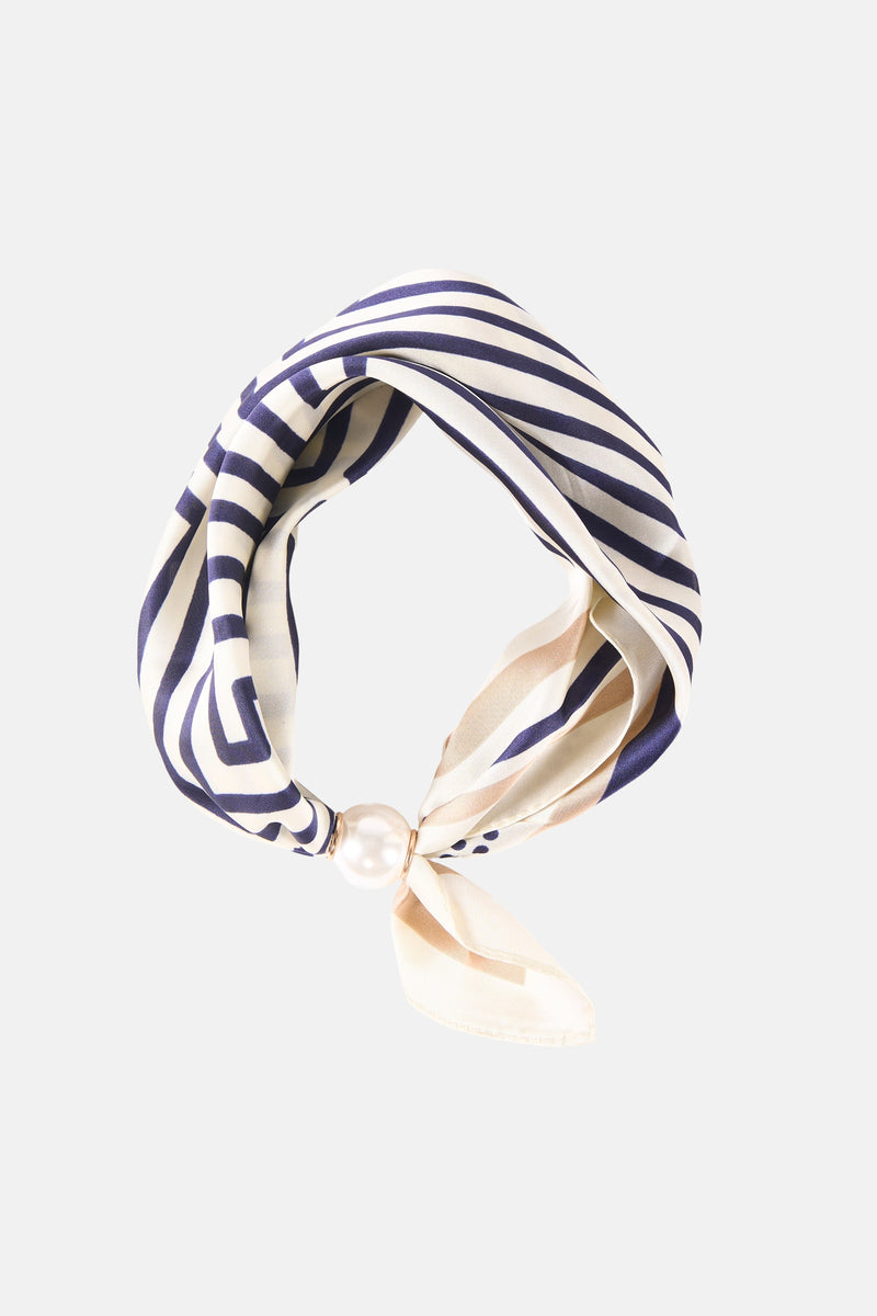Beige foulard with navy and cream stripes, featuring a pearl accent at the knot, styled in a looped fashion.
