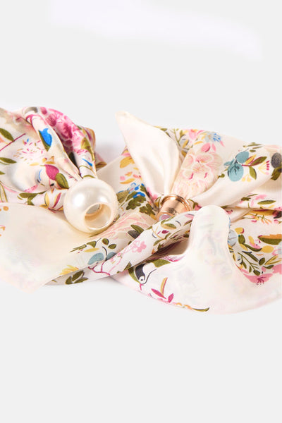 Multicolored floral foulard with cream base and pearl embellishment, tied in bow on white background