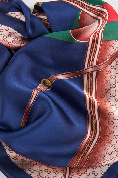 Navy blue silk foulard with bold geometric pattern, red and green accents, and repeating monogram border, shown in close-up detail.