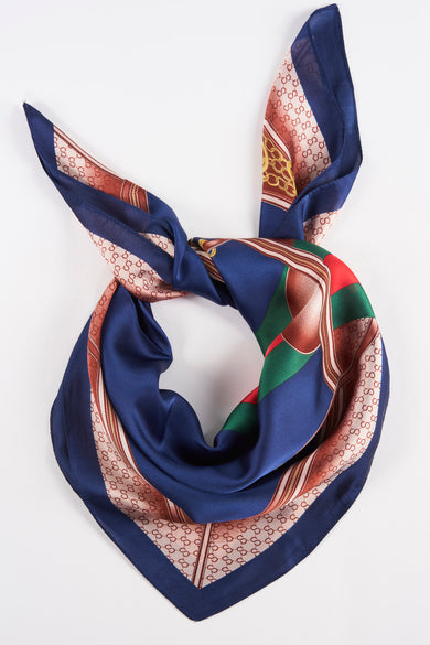 Navy blue silk foulard with repeating monogram pattern and colorful border, tied in a knot, top-down view