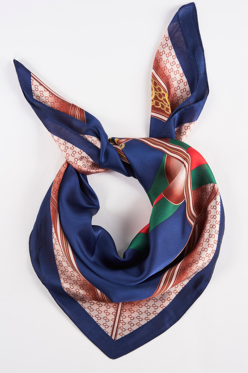 Navy blue silk foulard with repeating monogram pattern and colorful border, tied in a knot, top-down view