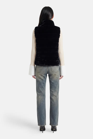 Veste sans manches noire d'Access® en fausse fourrure à bandes horizontales, vue de dos, sur un pull crème et un jean.