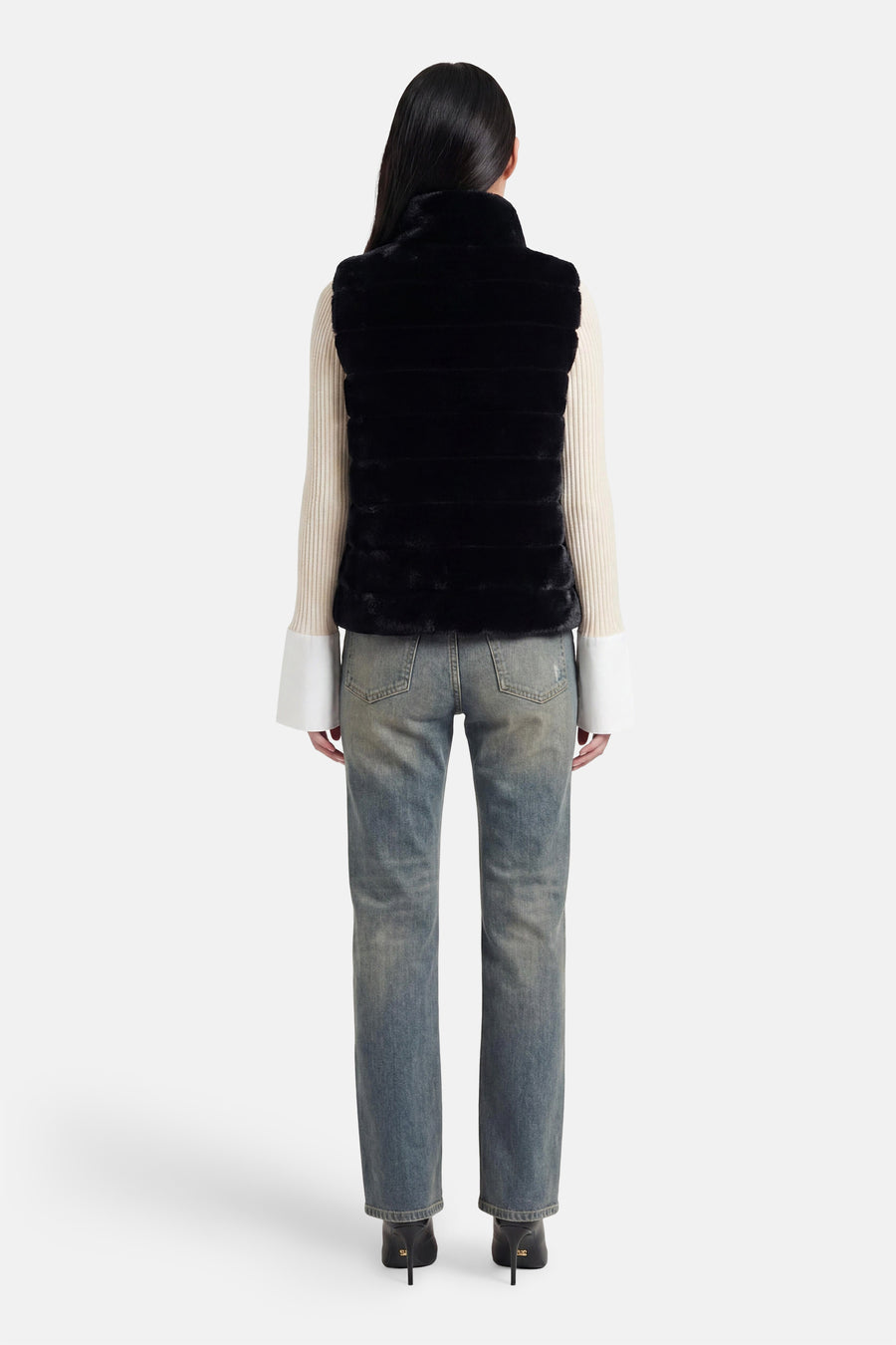 Veste sans manches noire d'Access® en fausse fourrure à bandes horizontales, vue de dos, sur un pull crème et un jean.