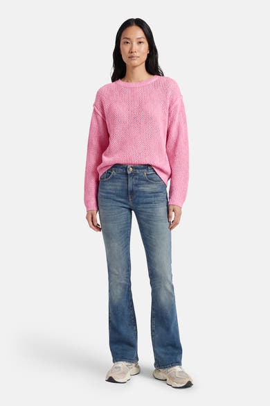 Pull rose à col rond d'ADORE, en maille texturée, porté avec un jean évasé et des baskets.
