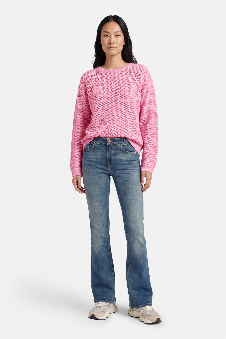 Pull rose à col rond d'ADORE, en maille texturée, porté avec un jean évasé et des baskets.

