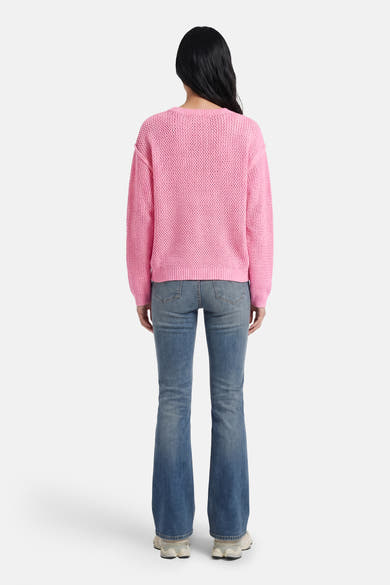 Pull rose à col rond par ADORE, porté avec un jean bootcut bleu.