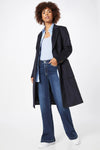 Jean évasé bleu de Le Temps des Cerises, porté avec un manteau long bleu marine, un chemisier bleu et des baskets blanches.