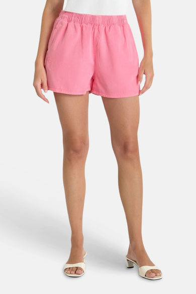 Korte roze rok van getextureerde stof van Le Temps des Cerises, met elastische tailleband en zakken, gedragen met lichte muiltjes.