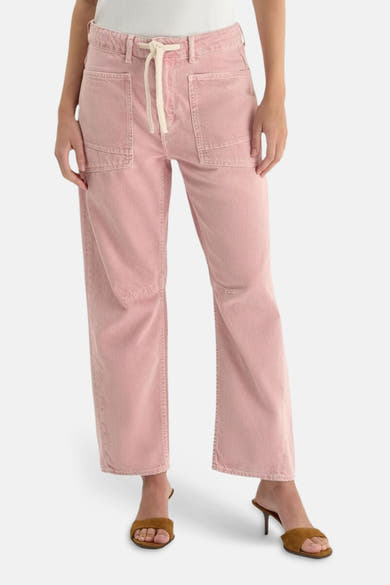 Jean coloré rose par Le Temps des Cerises, avec poches cargo et cordon de serrage, porté avec des mules marron.

