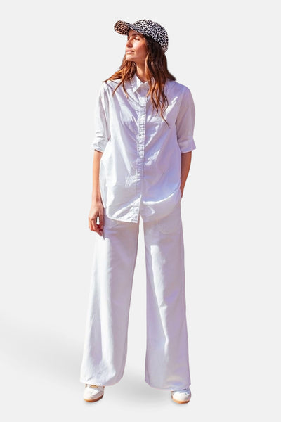 Jean large en denim blanc de Le Temps des Cerises, avec une chemise blanche, un chapeau à motif et des chaussures blanches.