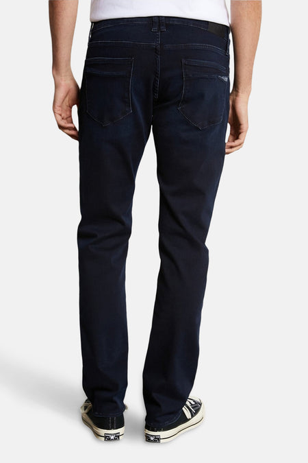 Jean droit en denim bleu noir de Le Temps des Cerises, avec poches arrière et chaussures noires et blanches.
