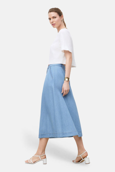 3/4 spijkerrok in lichtblauw van CAROLL, uitlopende pasvorm, gedragen met een witte crop top en witte sandalen.