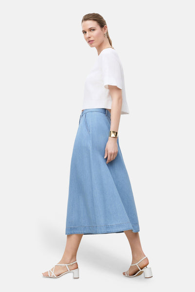 3/4 spijkerrok in lichtblauw van CAROLL, uitlopende pasvorm, gedragen met een witte crop top en witte sandalen.