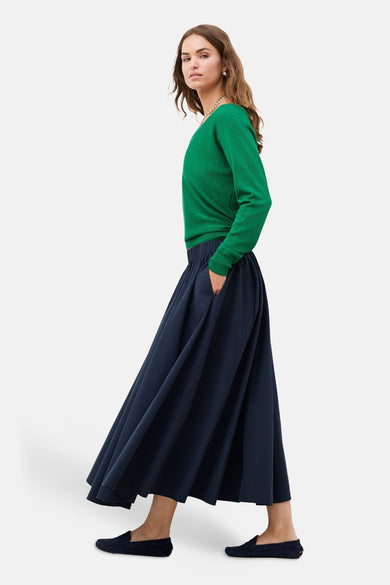 Lange blauwe rok van CAROLL met elastische taille, wijd en gedrapeerd, gedragen met een groene trui.