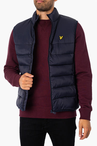 Veste sans manches bleu par LYLE & SCOTT, portée sur un pull bordeaux et un pantalon noir.