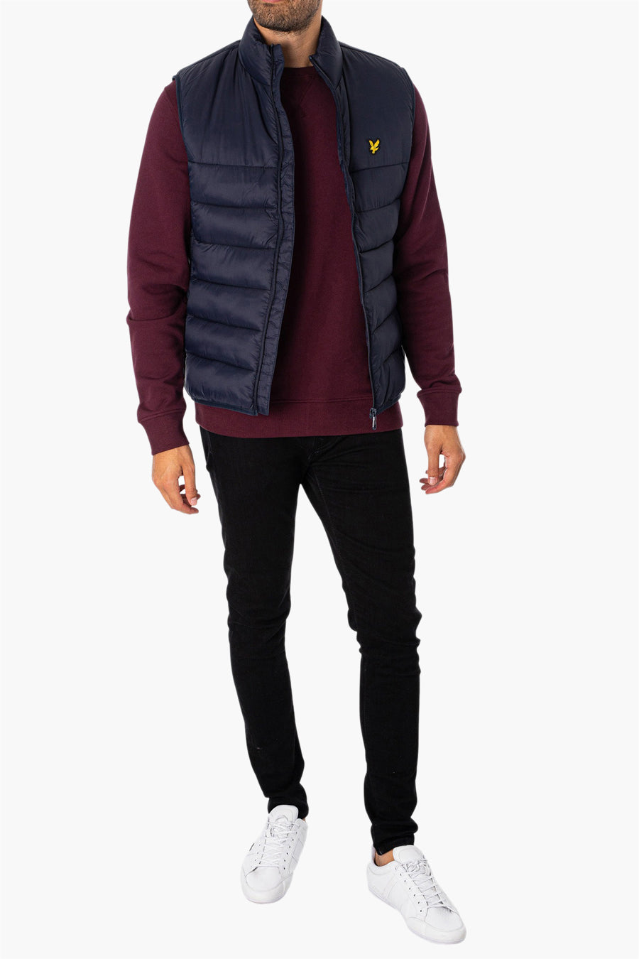 Veste sans manches bleue de LYLE & SCOTT, portée sur un pull bordeaux, avec un pantalon noir et des baskets blanches.