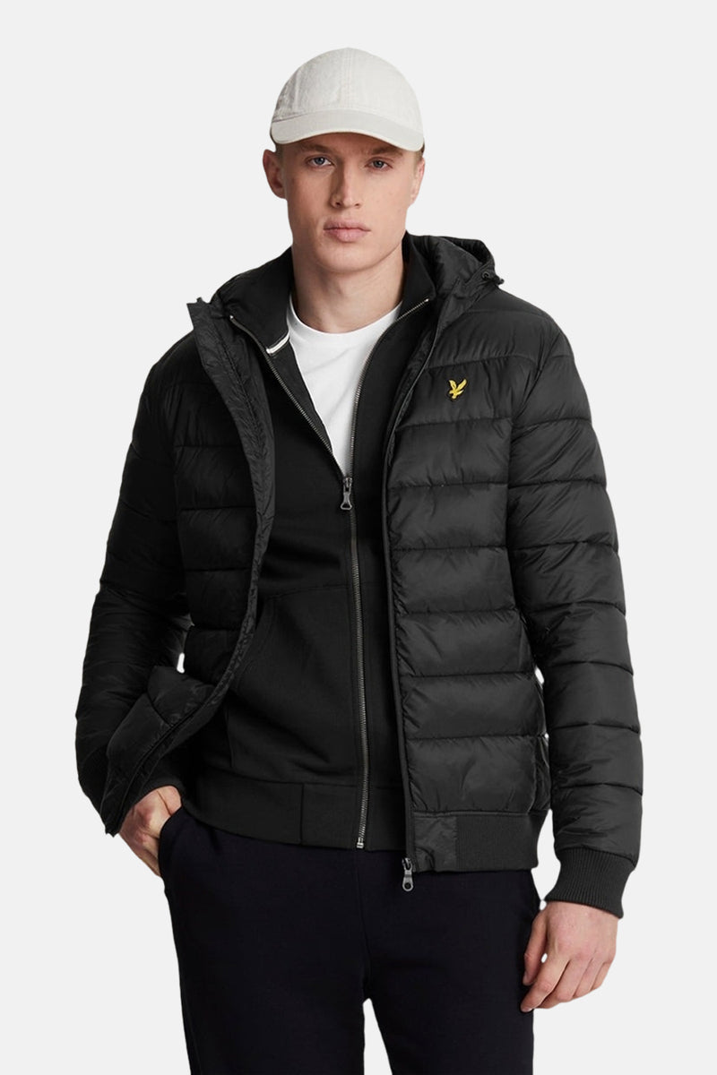 Veste courte noire de LYLE & SCOTT avec capuche, portée sur un sweat à capuche noir et un t-shirt blanc, avec un pantalon noir et une casquette blanche.